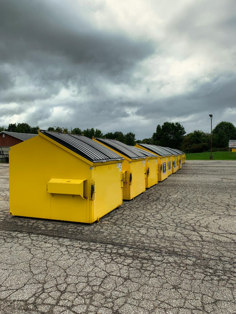 A series of yellow garbage bins lined up on a pavement under a cloudy sky in Wooster, OH.